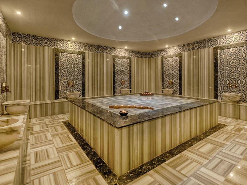Sala hammam lussuosa con marmo e pareti decorate, atmosfera calda ed elegante.