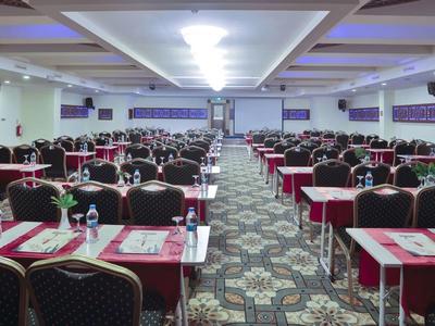 Grande sala conferenze con file di tavoli e sedie preparate per un evento.