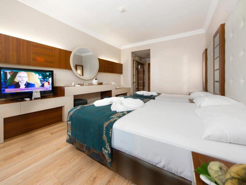 Camera moderna con letto grande, TV a muro e mobili in legno chiaro.