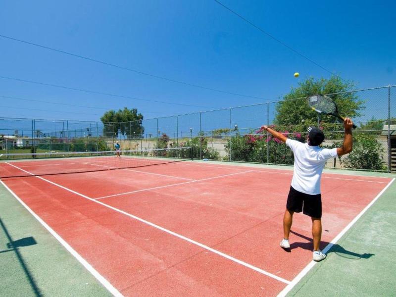 Persona su un campo da tennis rosso con cielo azzurro e alberi sullo sfondo.
