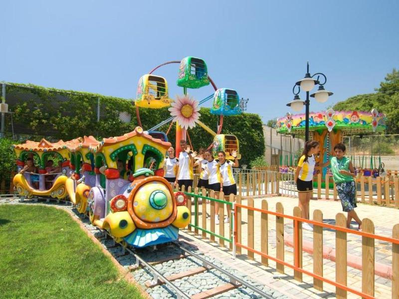 Un piccolo treno colorato in un parco giochi all'aperto con bambini che giocano.