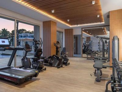 Salle de sport moderne avec tapis de course, haltères et grandes fenêtres donnant sur la piscine.