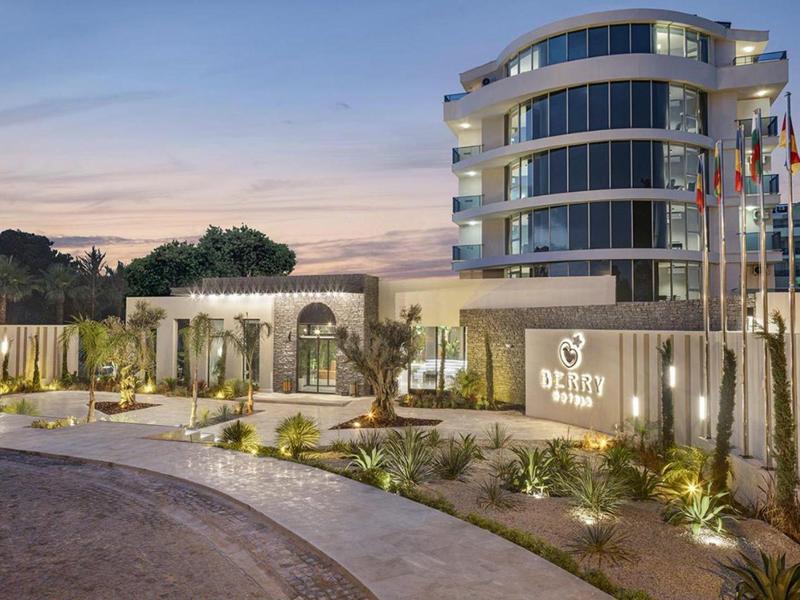 Bâtiment d'hôtel moderne avec entrée arrondie et aménagements extérieurs illuminés au coucher du soleil.