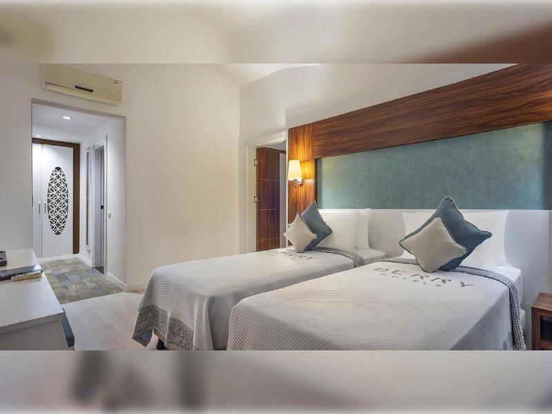 Chambre d'hôtel moderne avec deux lits simples, éléments en bois et éclairage subtil.