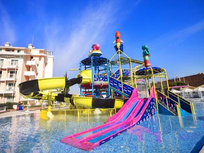 Park wodny z kolorowymi zjeżdżalniami i atrakcjami wodnymi obok budynków hotelowych pod błękitnym niebem.
