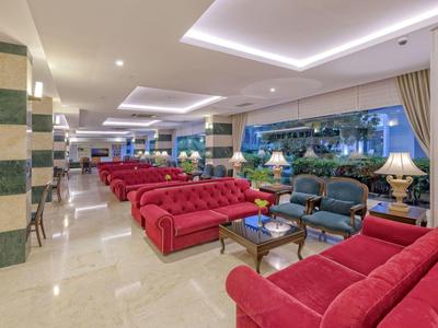 Duża przestrzeń hotelowego lobby z czerwonymi sofami, niebieskimi fotelami, jasnym oświetleniem i dużymi oknami.