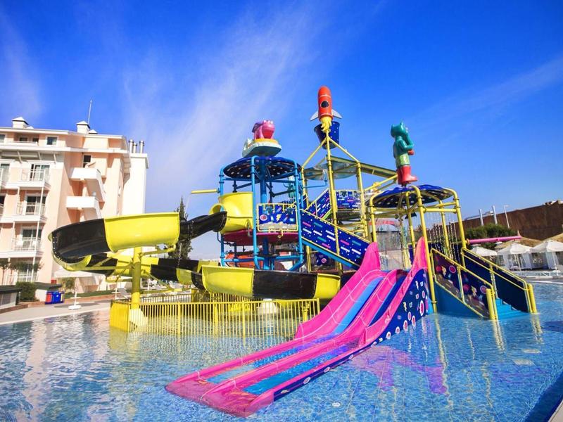 Buntes Wasserspiel mit Rutschen und Wasserpark unter blauem Himmel neben einem Wohnhaus.