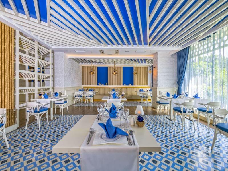 Helles Restaurant mit blau-weißen Tischen, gestreifter Decke und großen Fenstern.