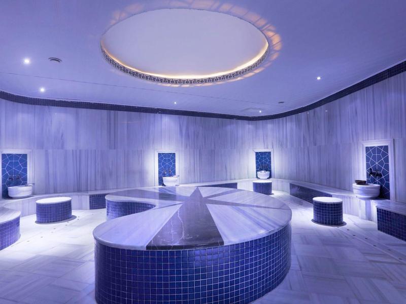 Moderner Raum mit rundem, blau gekacheltem Sitzbereich und kreisförmiger Deckenbeleuchtung.