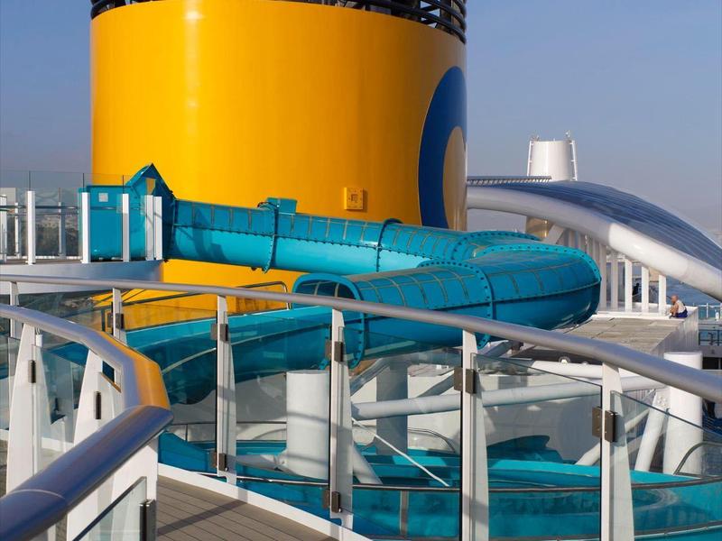 Gele schoorsteen met blauwe waterglijbaan op het dek van een cruiseschip bij heldere lucht.