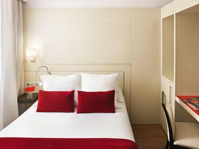 Nowoczesny pokój hotelowy z podwójnym łóżkiem, białą i czerwoną pościelą oraz minimalistycznym designem.