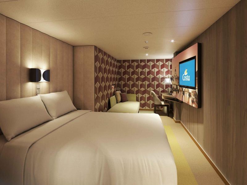 Habitación de hotel moderna con cama grande, silla cómoda y televisor en la pared en tonos cálidos.