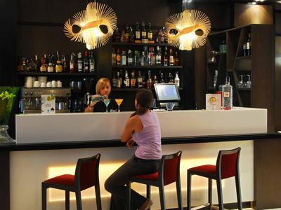 Modern hotel bar with bartender and guest at the counter with stylish lamps and drinks.