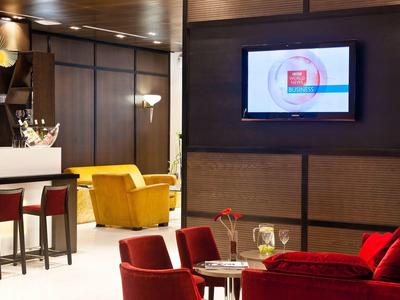Hotel lounge with red chairs, yellow armchair, and wall-mounted flat screen.