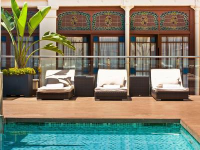 Three lounge chairs on a wooden deck beside a pool with green plants in the background