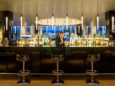 Bar moderno in hotel con illuminazione elegante, bottiglie e sgabelli in fila.