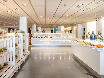 Area buffet luminosa e moderna con cibo fresco e piante decorative su scaffali bianchi.