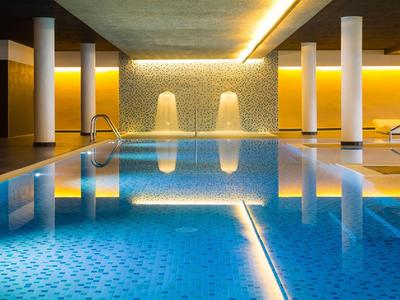 Innenraum-Schwimmbad mit beleuchtetem Wasser und modernen Säulen in warmem Licht.