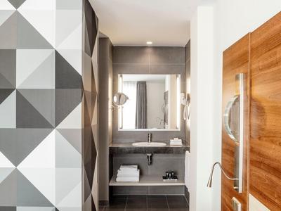 Camera d'hotel moderna con testiera in legno, comodino e parete con motivo geometrico.