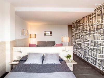 Modern hotel room with double bed, gray bedding, bedside lamps, and decorative wall art.