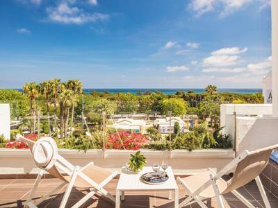 Two white lounge chairs and a small table on a terrace overlooking trees and the sea