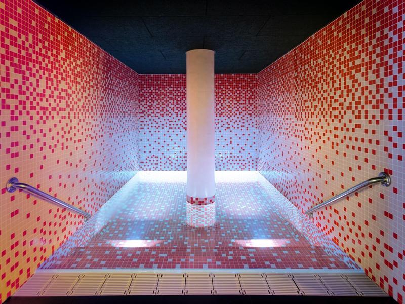 Modern spa bath area with pink mosaic tiles and heated water jets, featuring a central column.