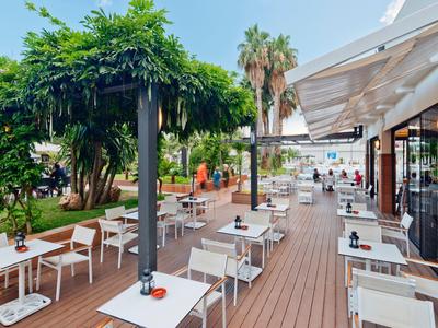 Outdoor cafe seating on wooden deck with green plants and umbrellas in sunny weather
