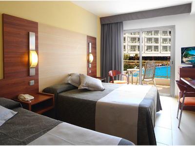 Hotel room with two beds, wooden furniture, and a balcony overlooking a pool.