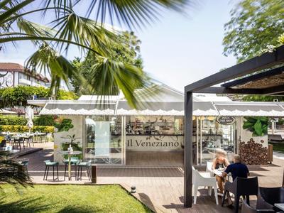 Outdoor restaurant seating with glass roof and palm trees in sunny weather.