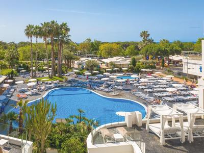 Large outdoor pool surrounded by sun loungers and palm trees in a hotel resort.