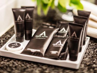 Luxury hotel toiletries arranged on a tray beside white towels and green plants.