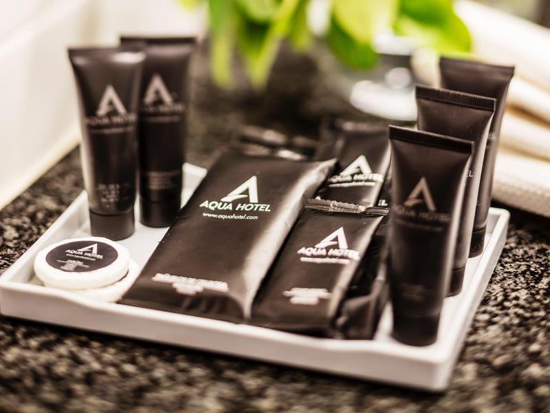 Luxury hotel toiletries arranged on a tray beside white towels and green plants.