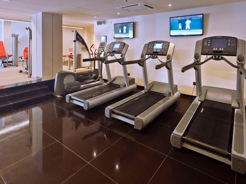 Moderne Fitnessraum mit drei Laufbändern, Spiegelwand, Fernsehern und glänzendem dunkelbraunem Boden.