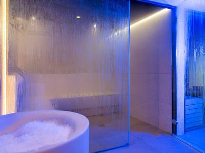 Area spa moderna con vasca idromassaggio, doccia in vetro e illuminazione blu.