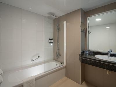 Hell gestaltetes Badezimmer mit Badewanne, großer Spiegel, weißen Fliesen und dunkler Arbeitsplatte.