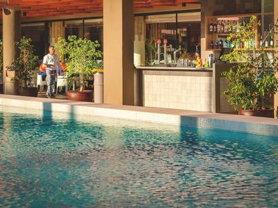 Ein Pool vor einer Bar mit Pflanzen und zwei Gästen in einem Hotelbereich.