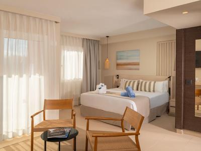 Bright hotel room with double bed, two wooden chairs, and large window with curtains.