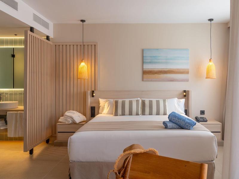 Camera d'albergo moderna con letto matrimoniale, lampade da comodino, divisori in legno e bagno sullo sfondo.