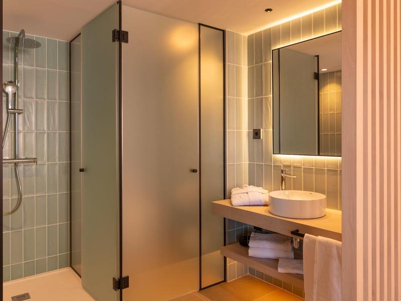 Bagno moderno in hotel con doccia, porta in vetro smerigliato, lavabo e specchio illuminato.