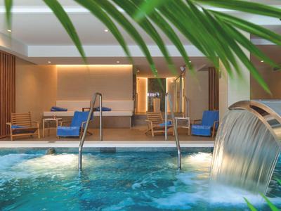 Vnitřní bazén s vodopádem a posezením v moderním lázeňském hotelu