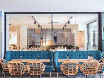 Area esterna moderna con panchine blu imbottite e tavoli in legno in un bar o hotel.