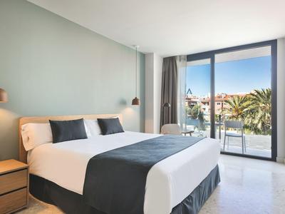 Brightly decorated hotel room with large bed and balcony overlooking palm trees.