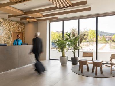 Hall dell'hotel con reception, personale, area salotto e grandi finestre con vista esterna.