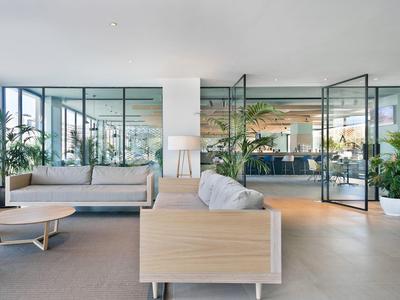 Moderna hall dell'hotel con pareti di vetro, divani beige, tavolini in legno e piante verdi.