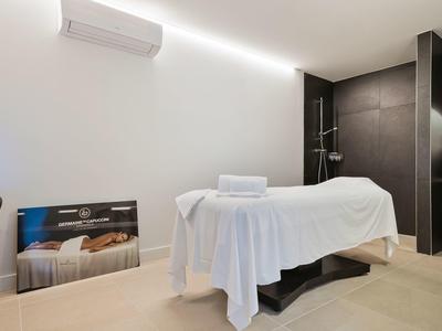 Modern spa room with massage table, white sheets, and dark tiled shower area.