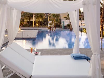 Relaxing poolside lounge bed under white canopy with a view of the swimming pool.