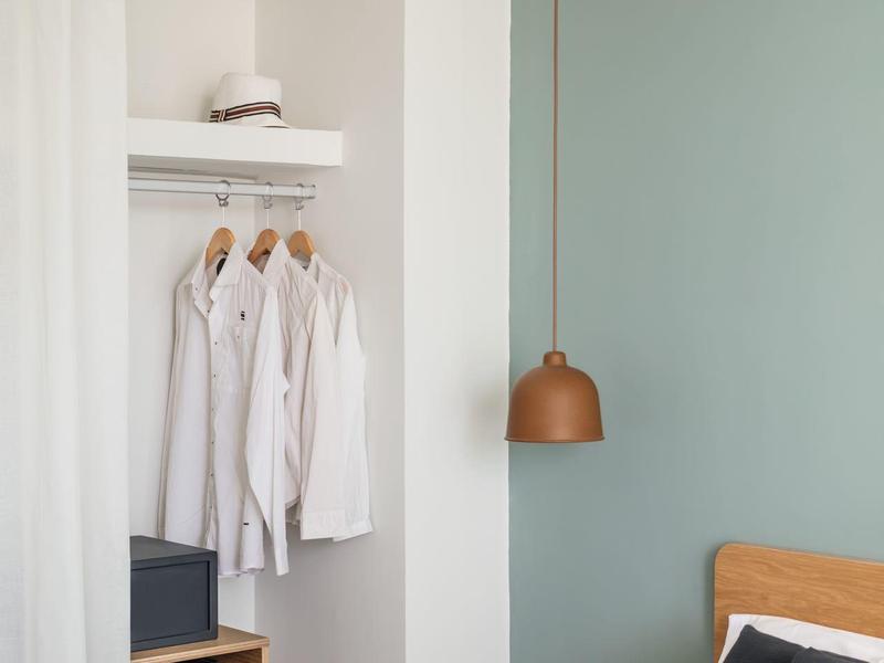 Cozy bedroom corner with wooden bed, white shirts hanging, and bedside table with decor.