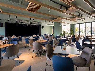 Spacious hotel dining room with modern tables, chairs, and large windows letting in natural light.