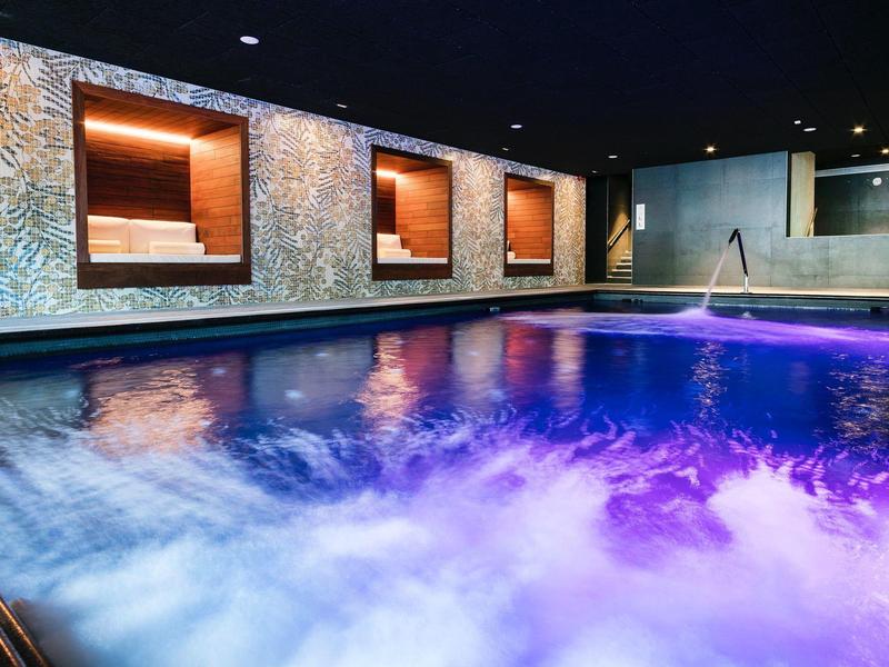 Indoor pool with colorful lighting and seating niches in a modern hotel spa.