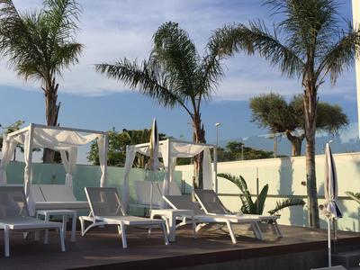 Outdoor lounge area with white sunbeds and cabanas by palm trees under clear sky.